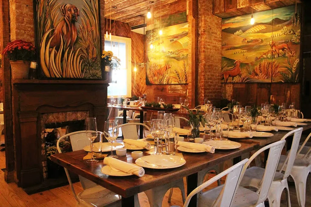 Empty rustic restaurant with set tables, exposed brick walls, and warm lighting.