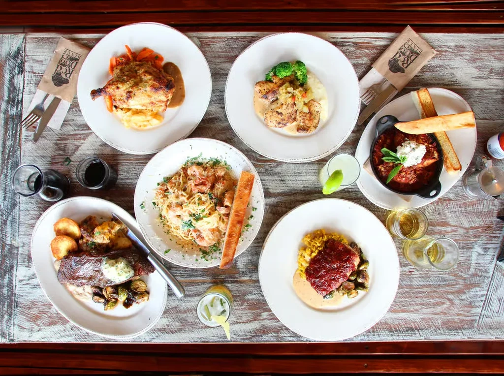 Six diverse plated meals, drinks, Red Dog Diner cutlery on a wood table.