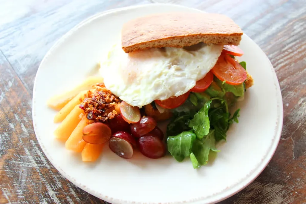 Breakfast toast with fried egg, tomatoes, avocado, and fresh fruit.