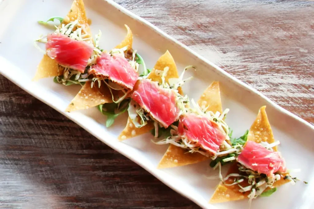 Five appetizers: seared tuna on crispy chips with greens on white dish.