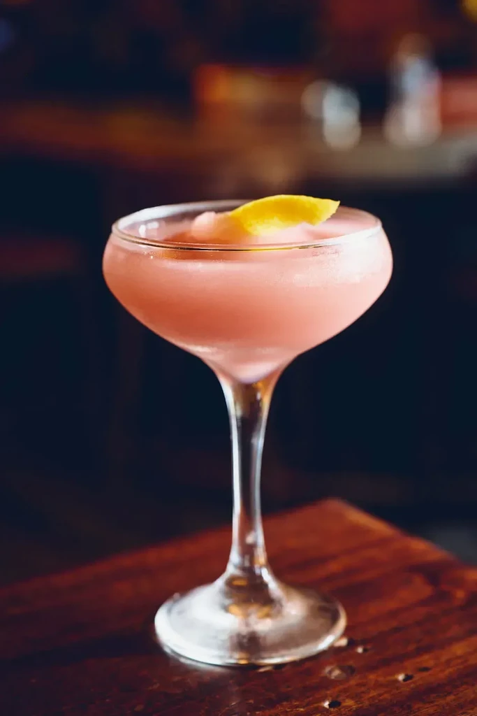 Pale pink slushy cocktail in coupe glass with lemon peel.