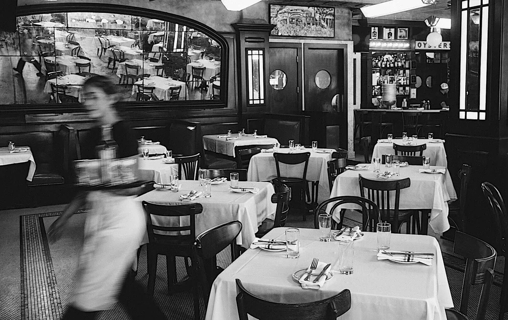 Black and white classic restaurant interior with a blurred server and bar.