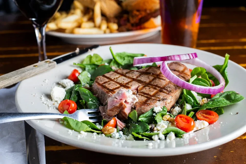 Grilled medium-rare steak with spinach, cherry tomatoes, cheese, and red onion.