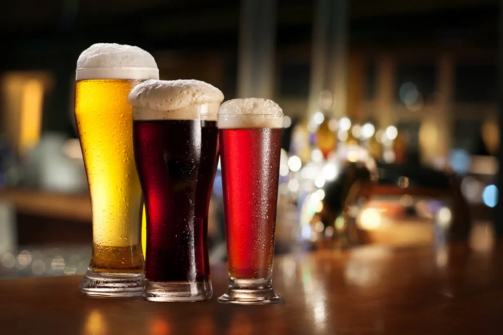 Three distinct beers, golden, brown, and amber, on a wooden bar.