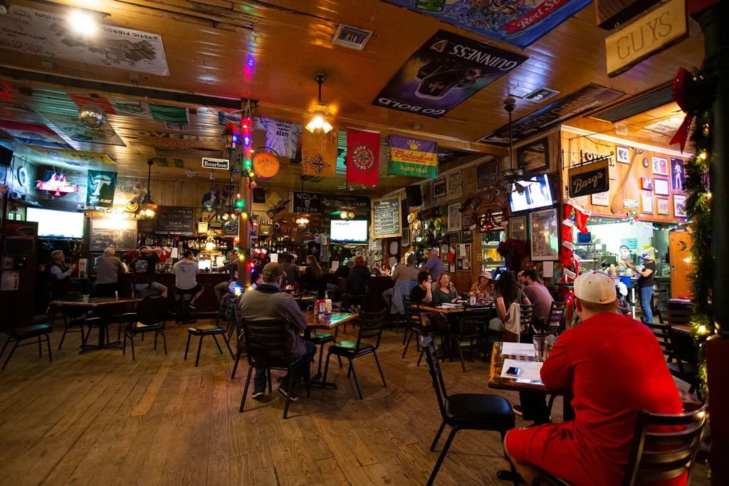 Rustic bar interior bustling with patrons, flags, signs, and sports TVs.