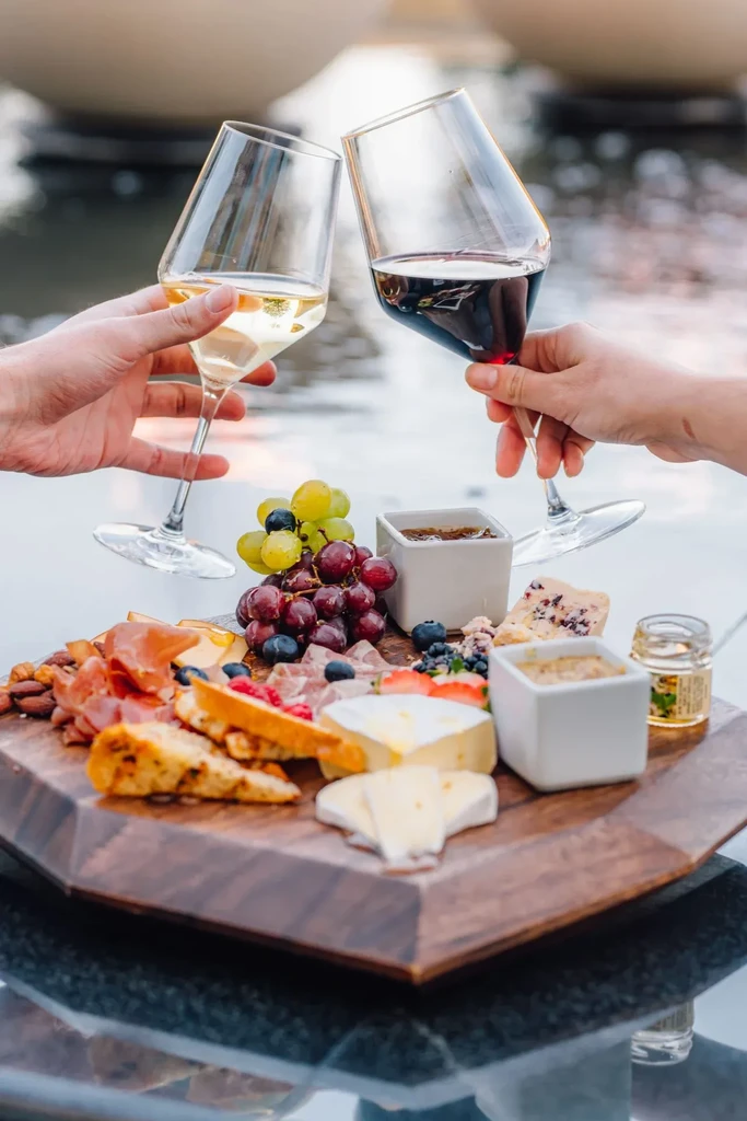 Outdoor charcuterie board with cheeses, meats, fruit, and wine toast.