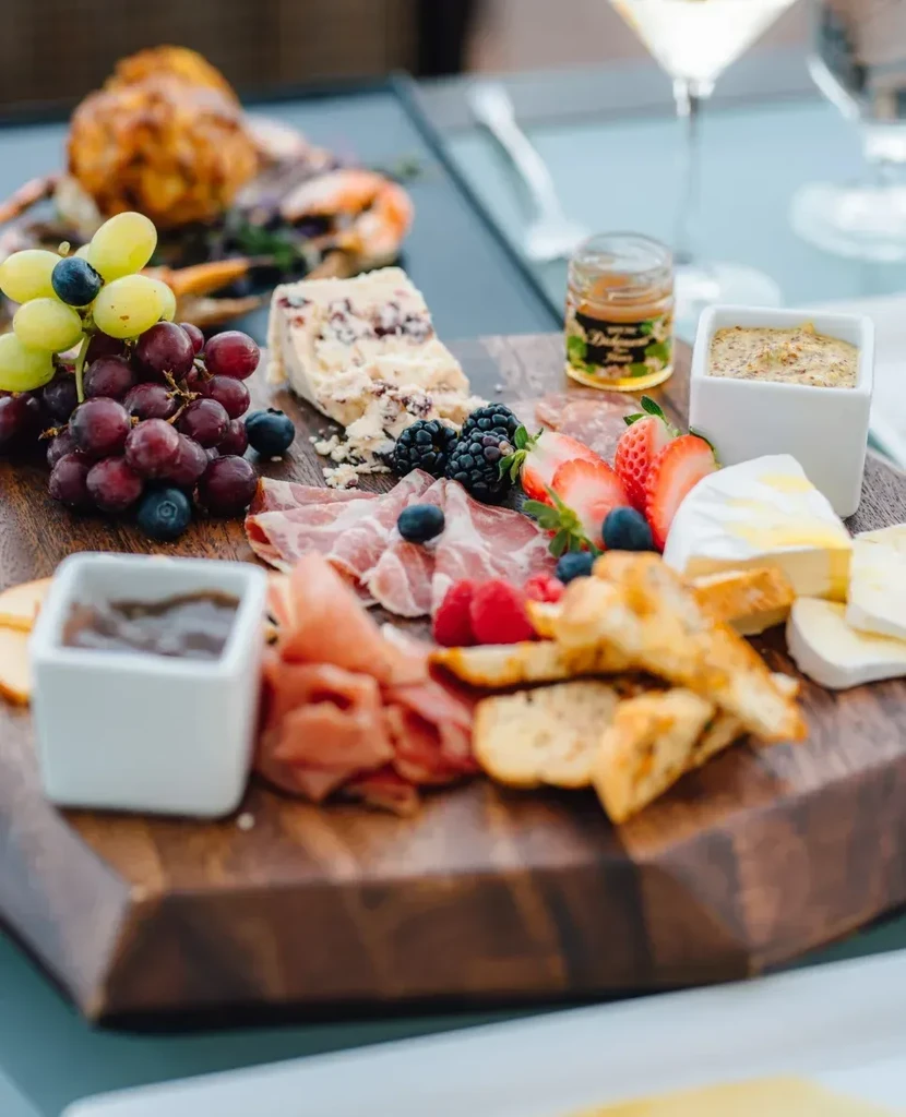 Rustic charcuterie board laden with cheeses, meats, fruit, crackers, and honey.