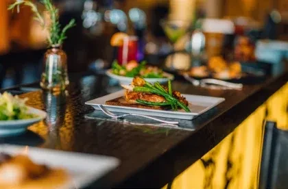 White plate with grilled protein and green vegetables on a dark counter.