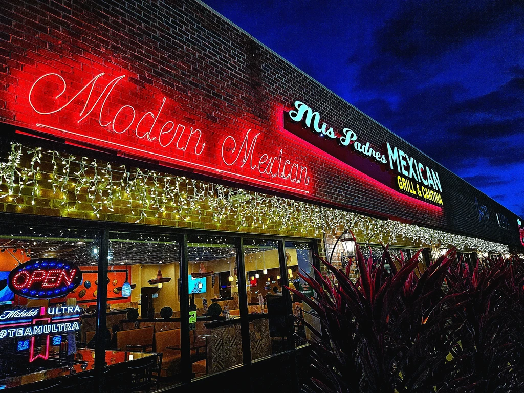 Mis Padres Mexican Grill exterior lit by colorful neon signs at night.