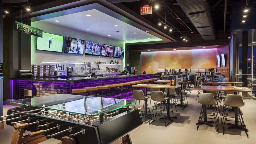 Lively modern restaurant with foosball, purple-lit bar, and abstract mural.