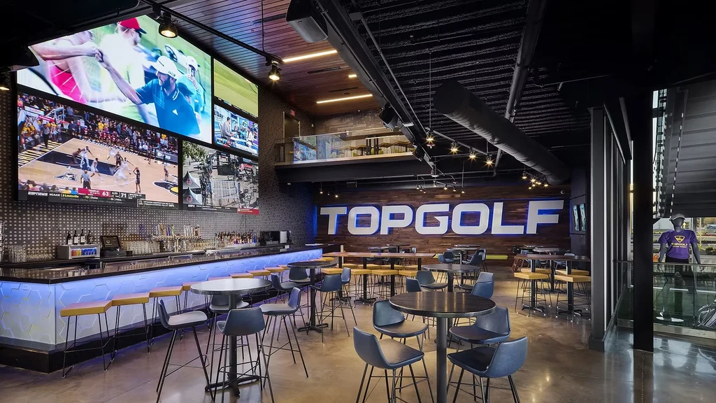 Topgolf's modern bar and dining area with sports screens, blue lighting.