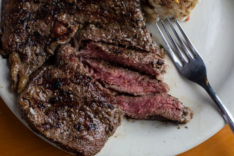 Sliced medium-rare steak with grill marks and fork on white plate.