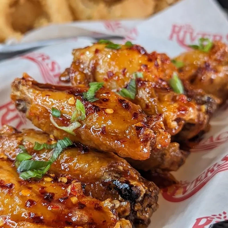Glazed chicken wings with red sauce, chili, and scallions in a basket.