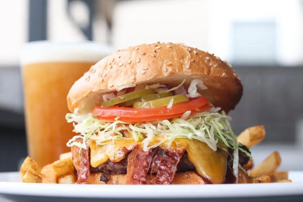 Gourmet burger with bacon, cheese, fries, and amber drink.