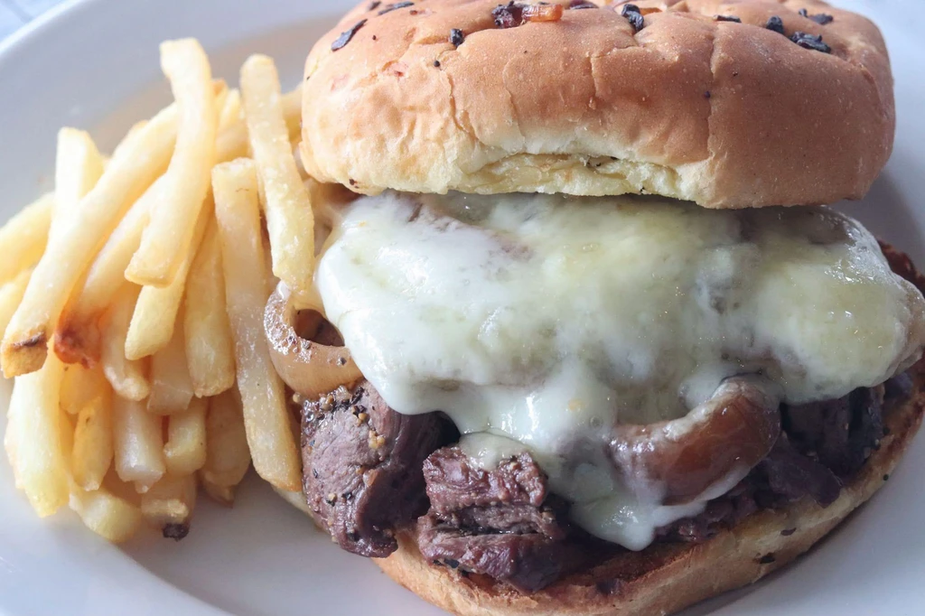 Melted cheese steak sandwich with caramelized onions and a side of fries.