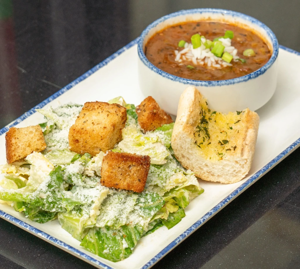 Full meal: stew, Caesar salad, and garlic bread on a white plate.