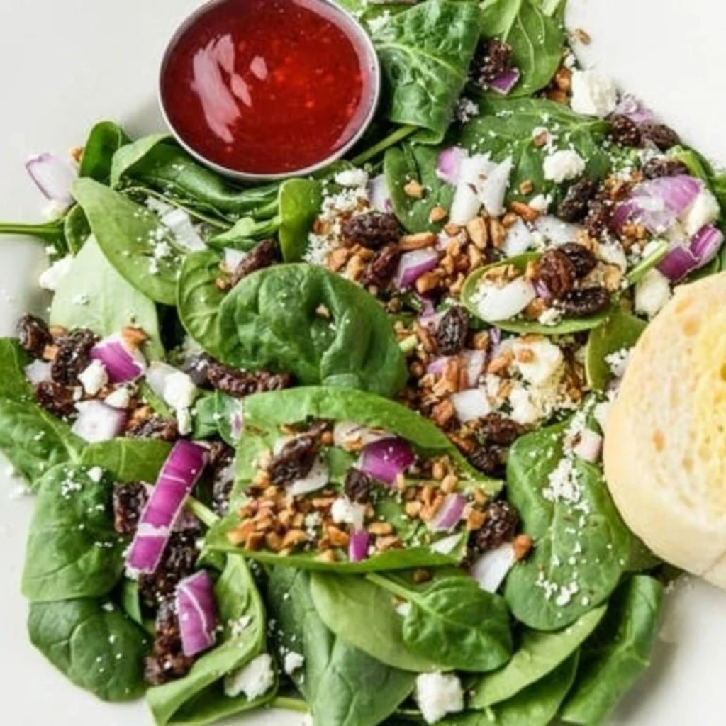 Spinach salad with feta, nuts, raisins, red onion, and berry dressing.