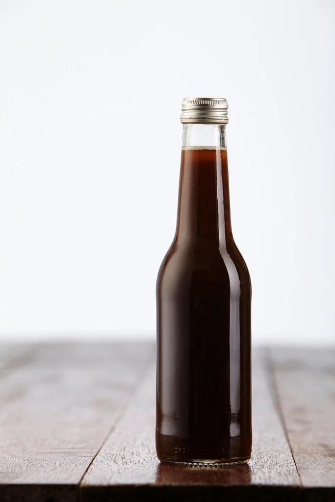 Glass bottle of dark brown beverage on a dark wooden surface.