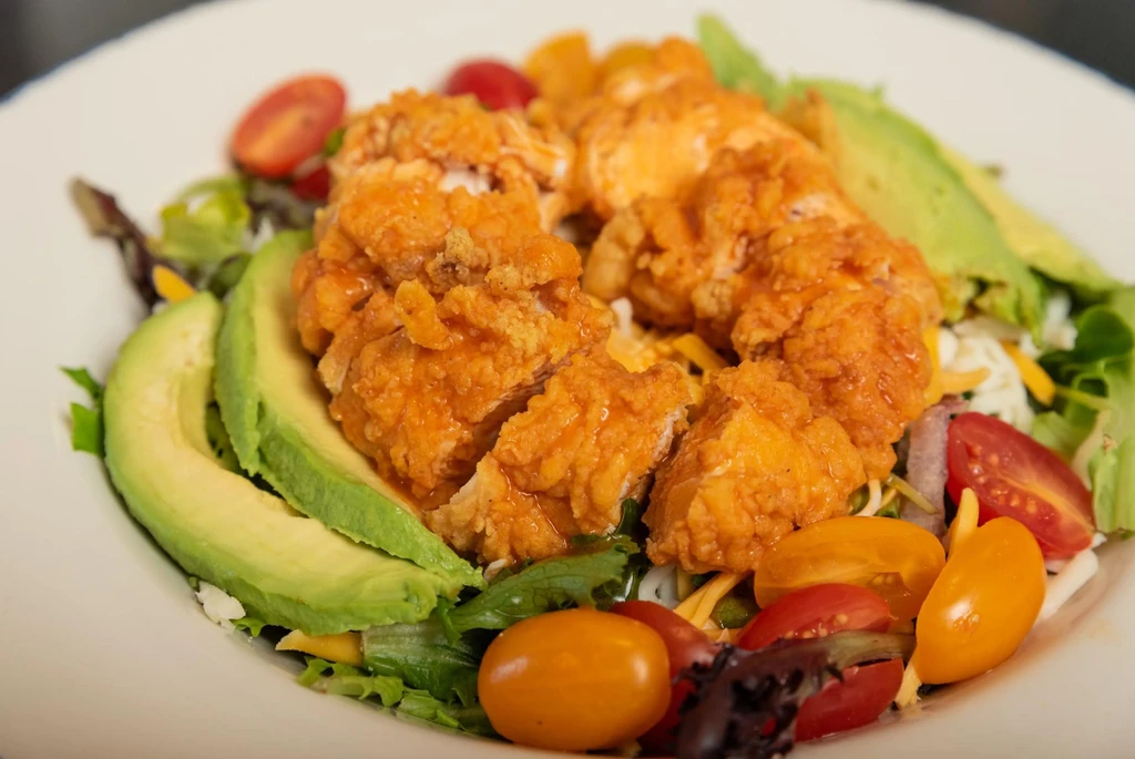 Fried chicken salad with avocado, lettuce, and tomatoes on a white plate.