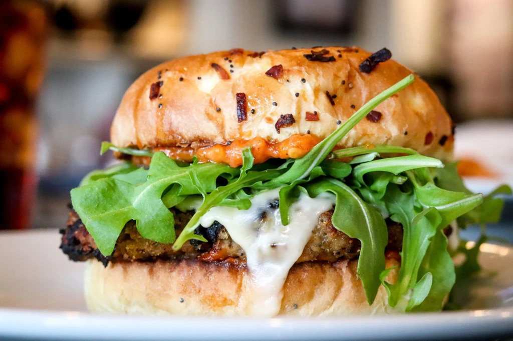 Gourmet burger with brioche bun, arugula, melted cheese, and grilled patty.