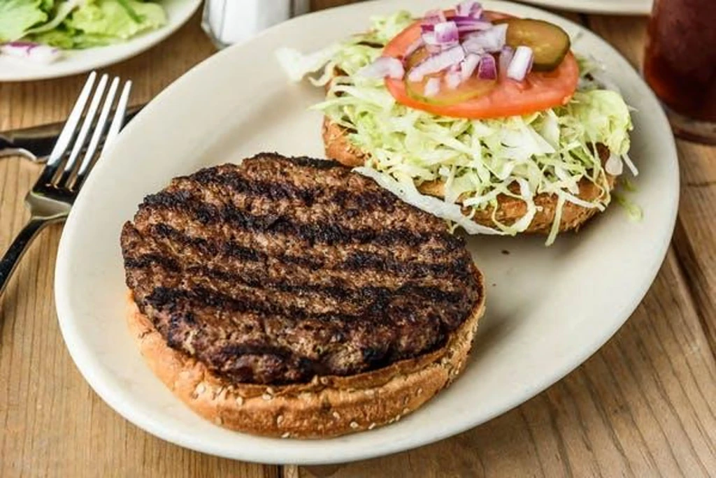 Deconstructed grilled burger with patty, bun, and toppings on a white plate.