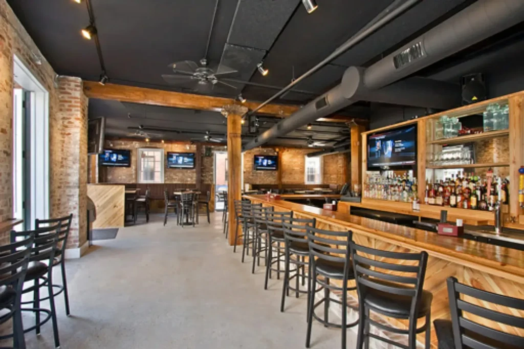 Spacious, empty industrial-rustic bar with brick walls and long wooden counter.