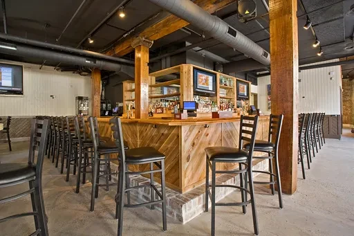 Long wooden bar in an empty rustic-industrial restaurant interior.