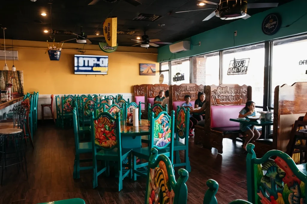 Interior of vibrant Chilangos Seafood restaurant with colorful carved chairs and patrons.