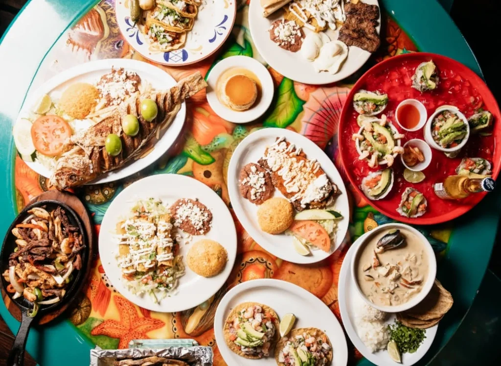 Top-down view: abundant, colorful Mexican and seafood dishes on a patterned table.