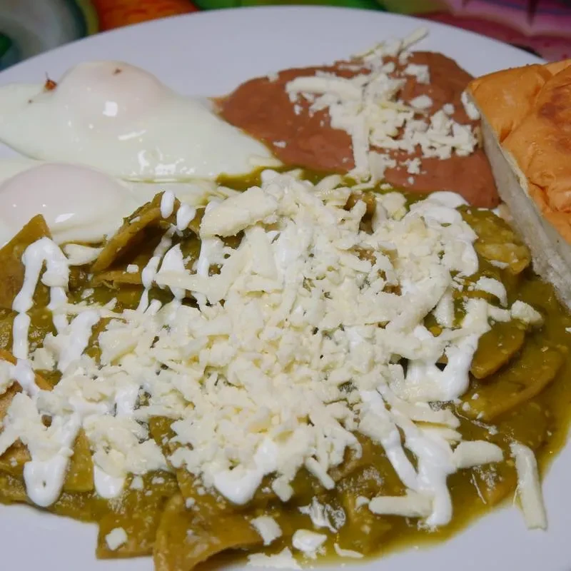 Chilaquiles verdes with fried eggs, refried beans, cheese, and bread.