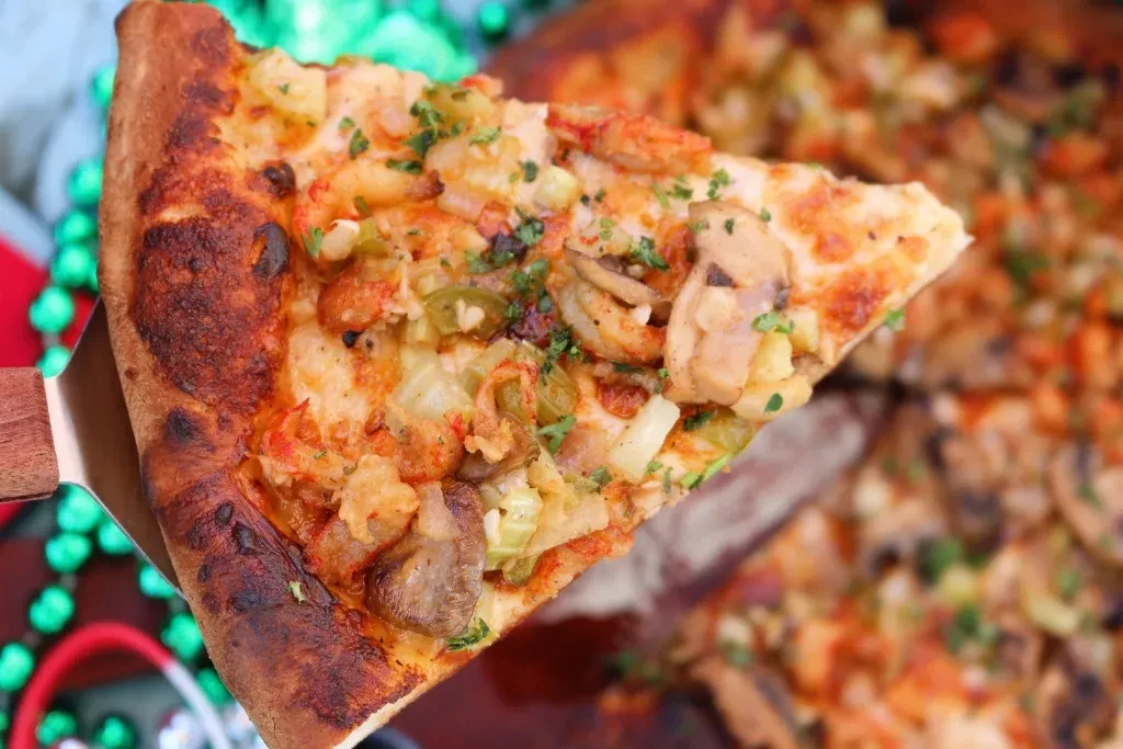 Pizza slice topped with shrimp, mushrooms, peppers, lifted by peel.