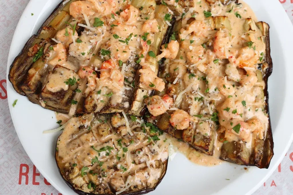 Overhead: Grilled eggplant with creamy seafood sauce, grated cheese, herbs.