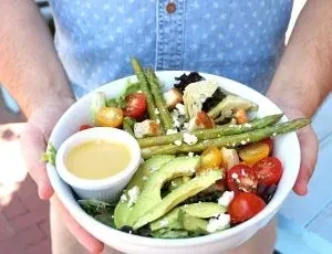 Fresh, colorful salad in white bowl with lettuce, tomatoes, avocado, feta.