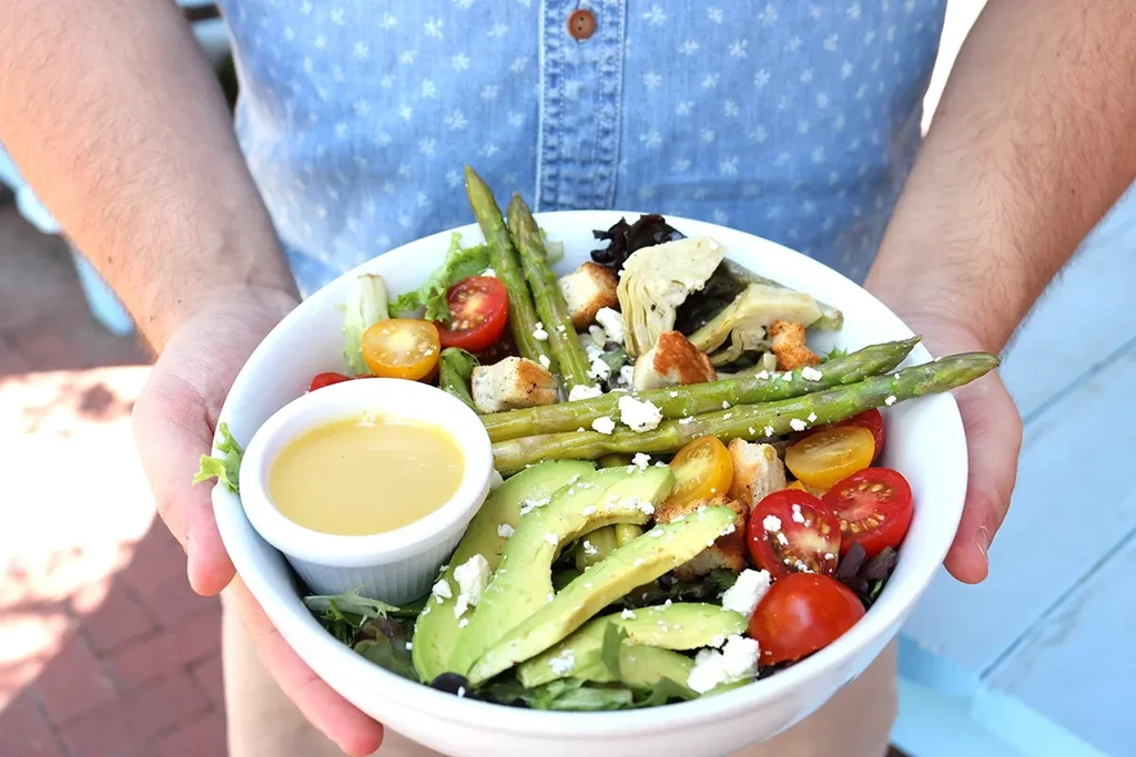 Vibrant salad with greens, avocado, tomatoes, cheese, held outdoors by person.