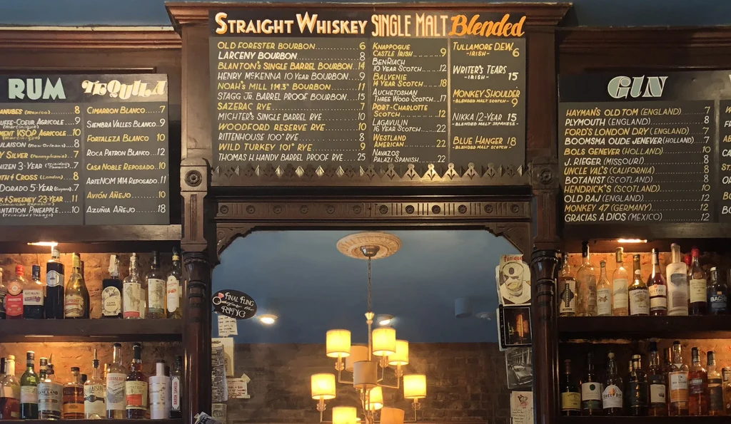 Rustic bar with chalkboard spirit menus and many liquor bottles.