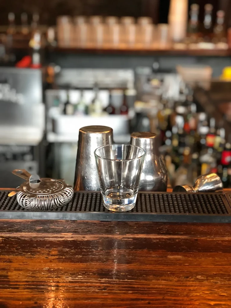 Warm wooden bar counter with cocktail tools on a black mat.