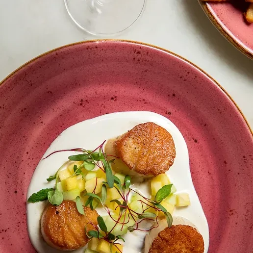 Overhead: Seared scallops on white sauce with diced fruit and fresh herbs.