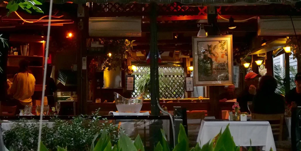 Warm restaurant interior with bar, plants, patrons, and Ferrano sign.