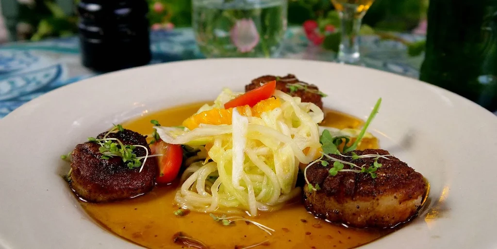 Seared scallops in sauce, with shredded salad, orange, and microgreens.