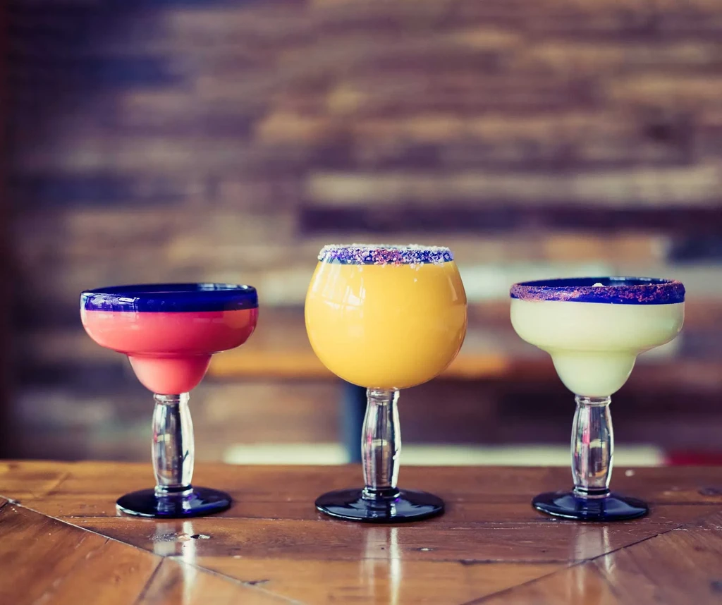 Three colorful drinks in distinct glasses on a wooden table.
