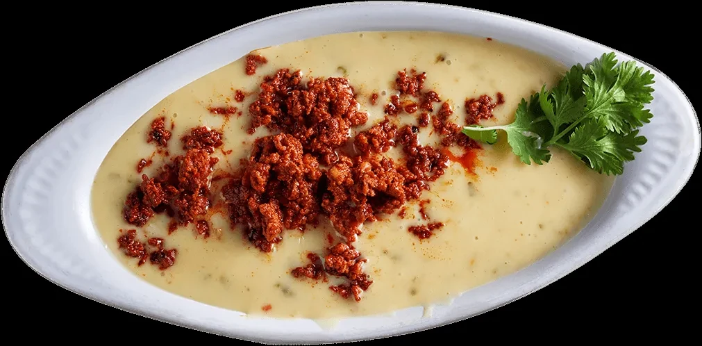 Oval white bowl of creamy queso, chorizo, and cilantro.