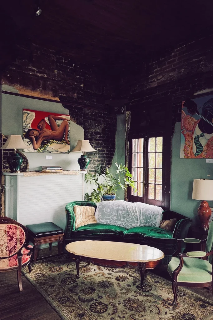 Richly decorated room with eclectic vintage furniture, art, and moody lighting.