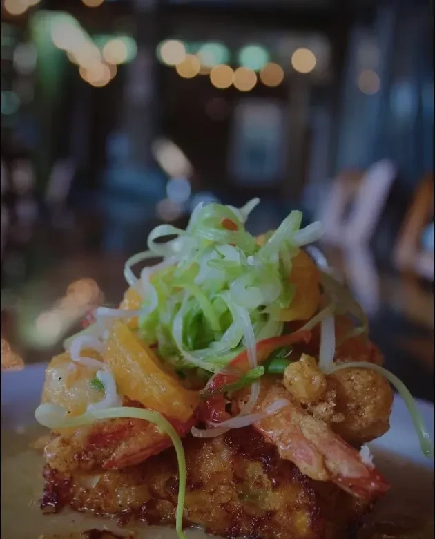 Close-up: Fried shrimp on crispy base, topped with greens and orange slices.