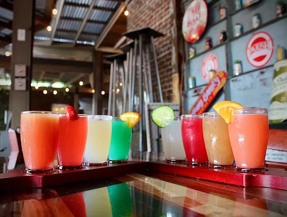Eight colorful cocktails garnished with fruit on wooden trays.