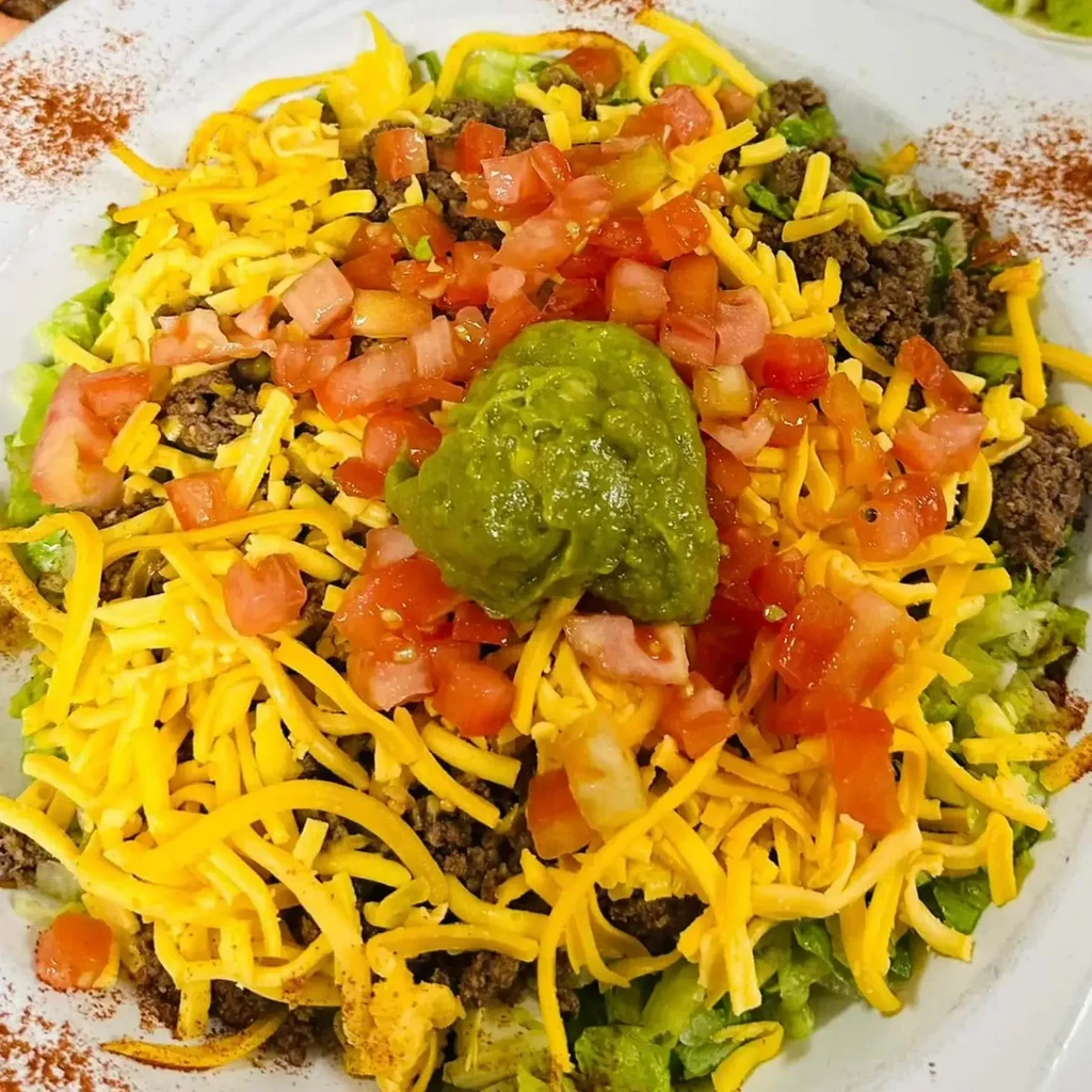 Taco salad with seasoned beef, cheddar cheese, lettuce, tomatoes, and guacamole.