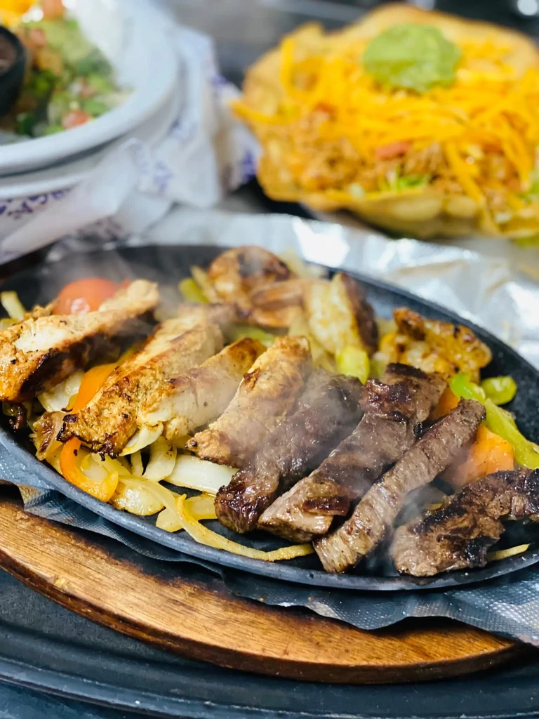 Sizzling chicken and beef fajitas with onions and peppers, steam rising.