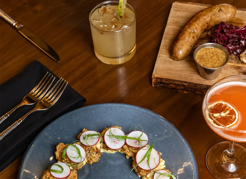 Overhead: dark table with cocktails, sausage, cabbage, and appetizers.