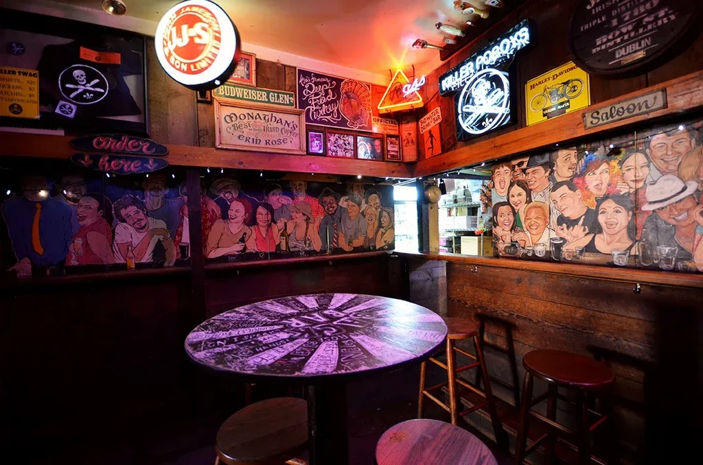 Wood-paneled bar with neon signs, cartoon faces, table, and bar stools.