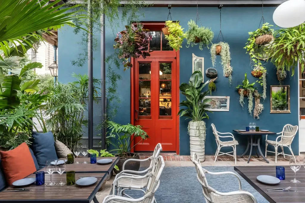 Lush botanical patio dining area with red doors and teal wall.