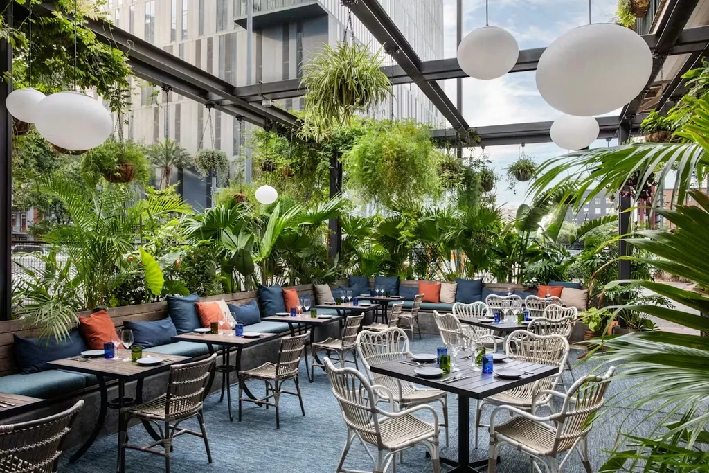 Vibrant plant-filled dining area set with tables, urban backdrop.